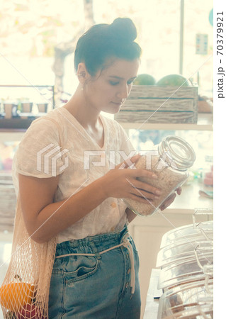 Young woman shopping in zero waste plastic free store with reusable mesh bag. Low waste lifestyle. Sustainable eco lifestyle Young woman shopping in zero waste plastic free store with reusable mesh bag. Low waste lifestyle. Sustainable eco lifestyle 70379921