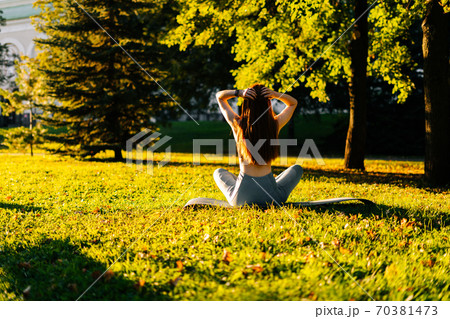 Back view of red-haired young woman sitting in lotus pose and hands up while meditating in yoga mat. Back view of red-haired young woman sitting in lotus pose and hands up while meditating in yoga mat. 70381473