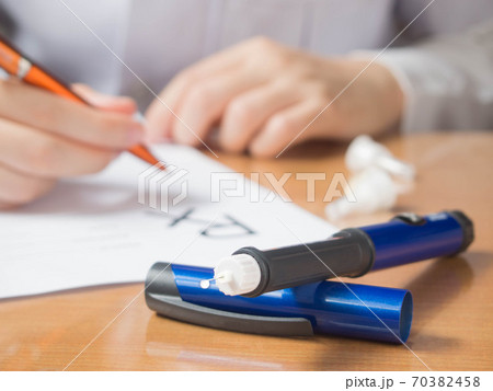 Close up of Insulin pen with insulin drop at needle tip on doctor table. Physician writing prescription to diabetes patient at hospital. World diabetes day. Health care medical concept. Close up of Insulin pen with insulin drop at needle tip on doctor table. Physician writing prescription to diabetes patient at hospital. World diabetes day. Health care medical concept. 70382458