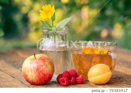 Ripe fruits, calendula flower with a stem in a glass jar and cup of greeen tea Ripe fruits, calendula flower with a stem in a glass jar and cup of greeen tea 70383417