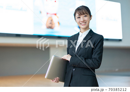 大型ビジョンの前にPCを持って立つ若いビジネスウーマン 大型ビジョンの前にPCを持って立つ若いビジネスウーマン 70385212
