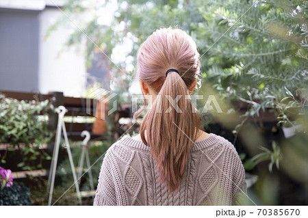 観葉植物に囲まれた 秋冬ニット服を来た綺麗な髪の女性の後ろ姿の写真素材