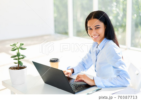 Smiling african american businesswoman sitting at her desk working on laptop Smiling african american businesswoman sitting at her desk working on laptop 70387713