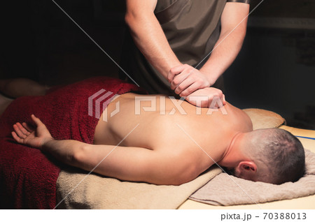Male masseur doing back massage to male client in a dark room 70388013