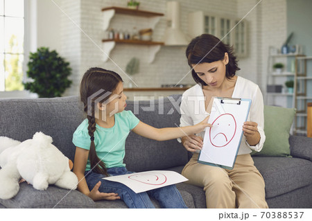 Pretty female child psychologist shows a little girl pictures with different emotions. Pretty female child psychologist shows a little girl pictures with different emotions. 70388537