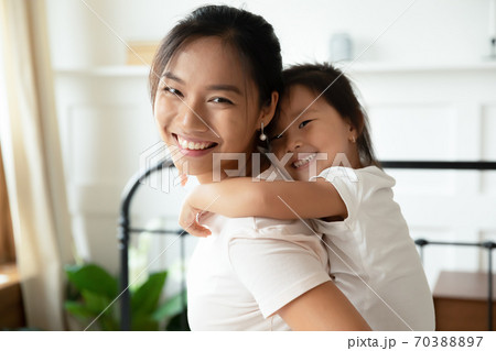 Head shot portrait smiling Asian mother piggy backing little daughter 70388897