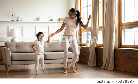 Overjoyed young Asian mother and little daughter dancing at home 70388937