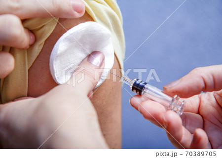 Hand of doctor holding syringe for vaccination to upper arm of patient Hand of doctor holding syringe for vaccination to upper arm of patient 70389705