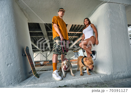 young stylishly dressed man and woman with an athletic figure with two american bully dogs under the bridge on city streets young stylishly dressed man and woman with an athletic figure with two american bully dogs under the bridge on city streets 70391127