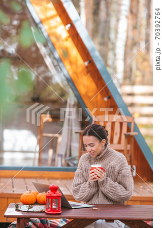 Happy young woman working on laptop and drinking coffee sitting at the wooden table outdoors Happy young woman working on laptop and drinking coffee sitting at the wooden table outdoors 70392764