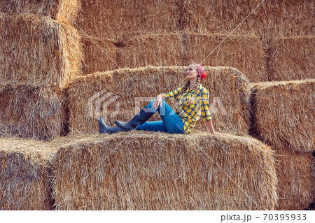Farmer woman having break on bale of straw Farmer woman having break on bale of straw 70395933