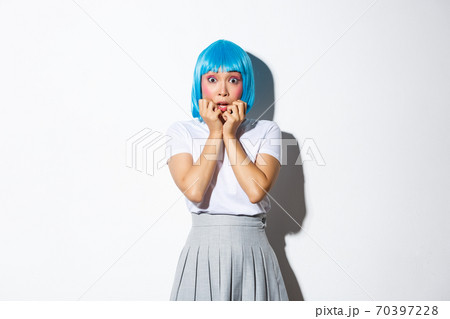 Portrait of scared asian woman gasping afraid, stare at camera ambushed, wearing blue party wig and schoolgirl uniform for halloween, standing over white background 70397228