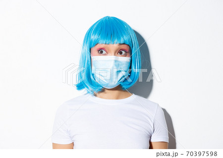 Concept of halloween celebration and coronavirus. Close-up of surprised cute asian woman in medical mask looking left at your logo, standing over white background 70397598