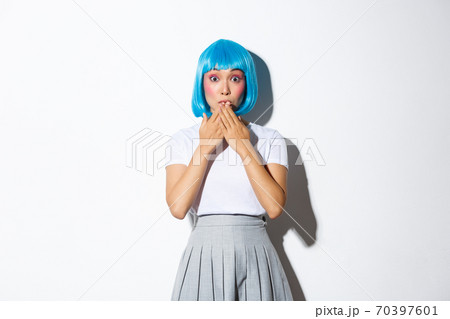 Portrait of surprised beautiful asian girl in glamour blue wig, looking amazed, holding hands near lips thrilled, standing over white background 70397601