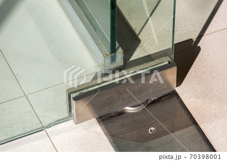 Glass door fittings, swivel mechanism holding the door metal loop on the tile floor close up. Glass door fittings, swivel mechanism holding the door metal loop on the tile floor close up. 70398001