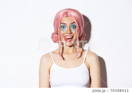 Close-up of attractive happy girl showing tongue and smiling, wearing pink party wig and bright makeup, standing over white background 70398413