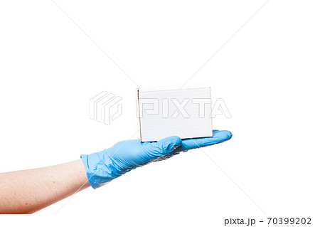 Delivery man's hand in a blue sterile latex glove holds a white unlabel cardboard box on palm, safe delivery during quarantine stay home, isolated on a white background with copy space. 70399202