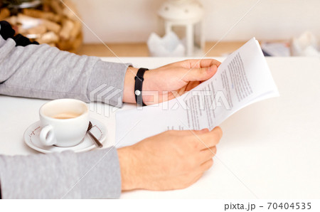 the man holds with both hands and reads the document on sheets of paper with coffee between his hands 70404535