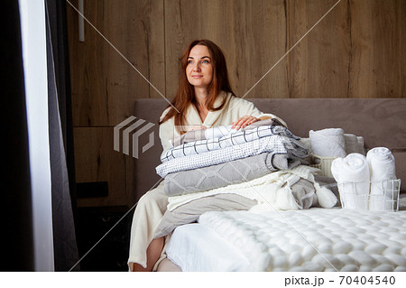 Young woman with beautiful smile in warm beige robe is leaning on stack of folded bed sheets 70404540