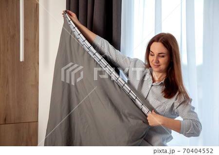 Happy woman with long red hair is folding clean bedding set on the bed of room with copy space. 70404552