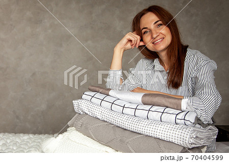 Beautiful woman in winter thick warm robe is sitting and neatly folding bed linens and bath towels Beautiful woman in winter thick warm robe is sitting and neatly folding bed linens and bath towels 70404599
