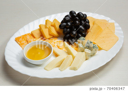 five sorts of cheese are laid out on a plate, cut into pieces, a bunch of grapes and honey in a bowl lie next to it, an assortment of cheese five sorts of cheese are laid out on a plate, cut into pieces, a bunch of grapes and honey in a bowl lie next to it, an assortment of cheese 70406347