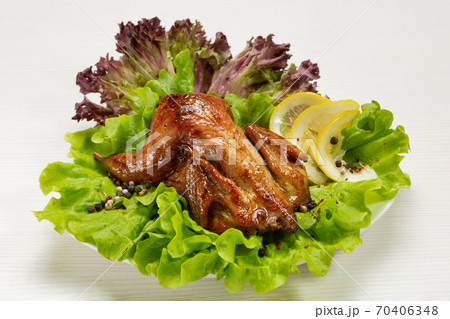 grilled quail lies on a plate, on green lettuce, next to slices of lemon and spices, on a table grilled quail lies on a plate, on green lettuce, next to slices of lemon and spices, on a table 70406348