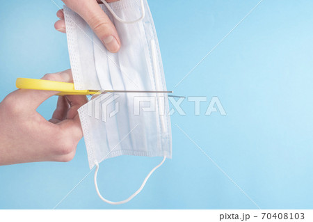 Man cuts a medical protective mask with yellow scissors on a blue background. Copyspace. The idea of conspiracy and disbelief in the danger of coronavirus 70408103
