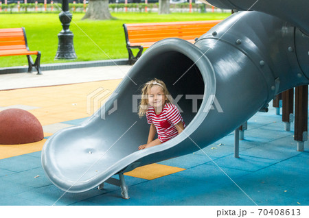 Cute little kid girl excitedly plays on playground slide on a cool sunny day. Happy kid outdoors. Cute little kid girl excitedly plays on playground slide on a cool sunny day. Happy kid outdoors. 70408613
