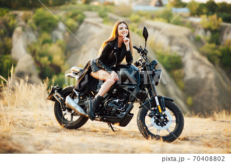 Girl on a motorcycle. She is beautiful, posing on a motorcycle at sunset Girl on a motorcycle. She is beautiful, posing on a motorcycle at sunset 70408802