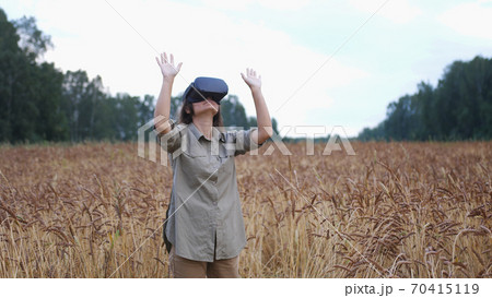 Beautiful girl in a golden wheat field uses virtual reality glasses 70415119