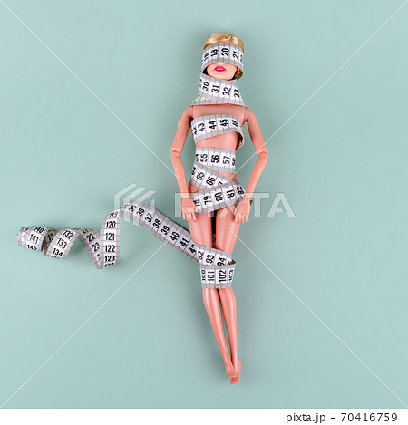 Doll wrapped in measuring tape. Tied up unrecognizable plastic doll, weight loss, fasting and slimming, diet, anorexia, overeating control, female fight for perfect fit body concept. Free copyspace 70416759