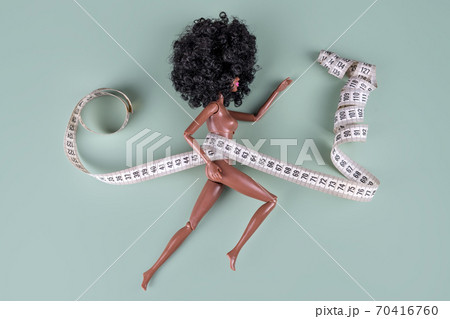 Doll wrapped in measuring tape. Tied up unrecognizable plastic doll, weight loss, fasting and slimming, diet, anorexia, overeating control, female fight for perfect fit body concept. 70416760