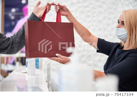 Responsible saleswoman in a mask holding a product bag Responsible saleswoman in a mask holding a product bag 70417334