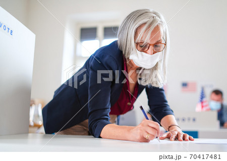 Portrait of woman voter with face mask in polling place, elections and coronavirus concept. Portrait of woman voter with face mask in polling place, elections and coronavirus concept. 70417481