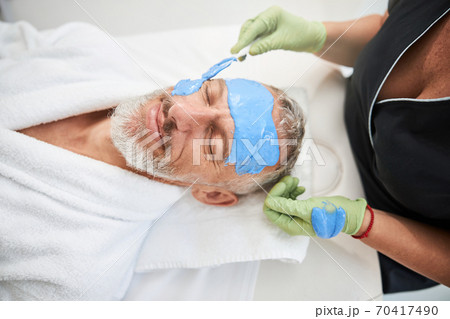 Relaxed senior man has his faced covered in blue cream 70417490