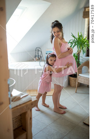 Portrait of pregnant woman with small daughter indoors at home, hugging. Portrait of pregnant woman with small daughter indoors at home, hugging. 70417589
