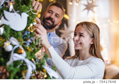 Happy couple indoors at home at Christmas, decorating tree. Happy couple indoors at home at Christmas, decorating tree. 70417648
