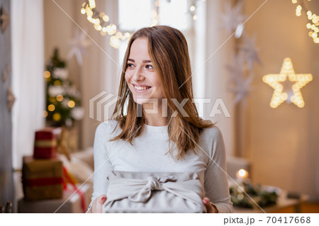 Happy young woman indoors at home at Christmas, holding present. 70417668