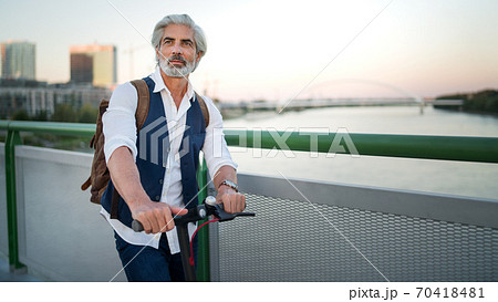 Mature man commuter with electric scooter outdoors in city, going to work. Copy space. Mature man commuter with electric scooter outdoors in city, going to work. Copy space. 70418481