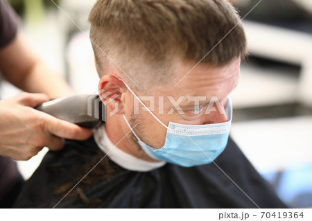 Young man in protective mask on face makes haircut in beauty salon portrait 70419364