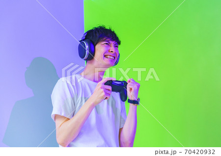 【eスポーツのイメージ】紫と緑の照明のもとコントローラを持ってエキサイトしている男性ゲーマー 【eスポーツのイメージ】紫と緑の照明のもとコントローラを持ってエキサイトしている男性ゲーマー 70420932