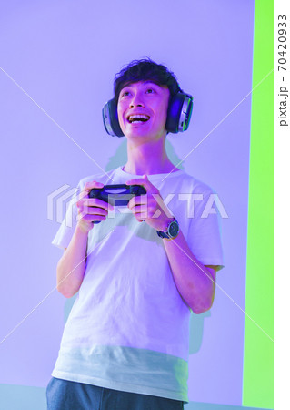 【eスポーツのイメージ】紫と緑の照明のもとコントローラを持ってエキサイトしている男性ゲーマー 【eスポーツのイメージ】紫と緑の照明のもとコントローラを持ってエキサイトしている男性ゲーマー 70420933