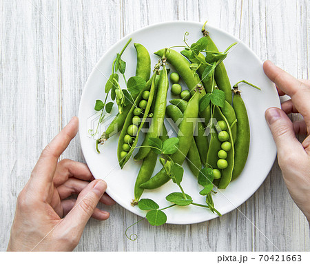 Green peas in a plate on a white wooden  background. View from above. 70421663