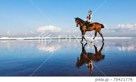 Woman riding horse on beach along sea by water pool. 70421776