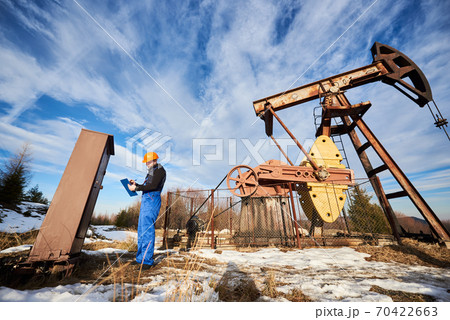 Oil well operator working in oil field with pump jack. Oil well operator working in oil field with pump jack. 70422663