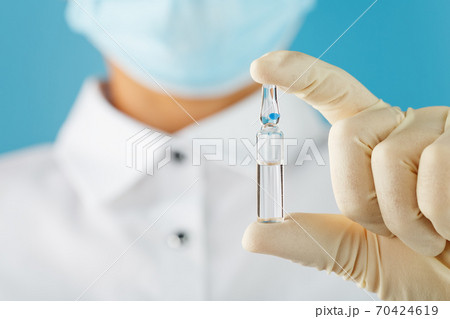 In the hands of a research scientist, a doctor in rubber gloves, an ampoule with a vaccine close-up. In the hands of a research scientist, a doctor in rubber gloves, an ampoule with a vaccine close-up. 70424619