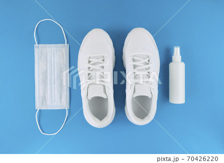 White medical mask, trainers, and hand sanitizer on a blue background. Monochrome flat lay. Quarantine outfit. White medical mask, trainers, and hand sanitizer on a blue background. Monochrome flat lay. Quarantine outfit. 70426220