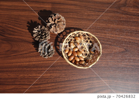 テーブルの上の松ぼっくりと籠に入ったドングリ 70426832
