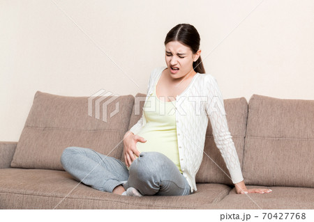 Pregnant woman with painful belly on sofa at home Pregnant woman with painful belly on sofa at home 70427768